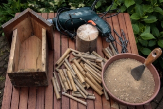 1/ Benodigdheden: een oud nestkastje zonder voorzijde, bamboestukjes, een stuk dikke tak, leem en een boormachine met houtboren.